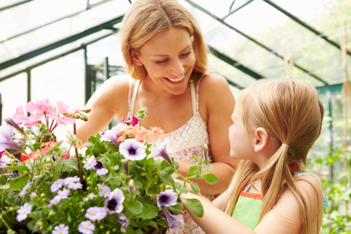 Mother And Daughter Growing Plants In Greenhouse Together