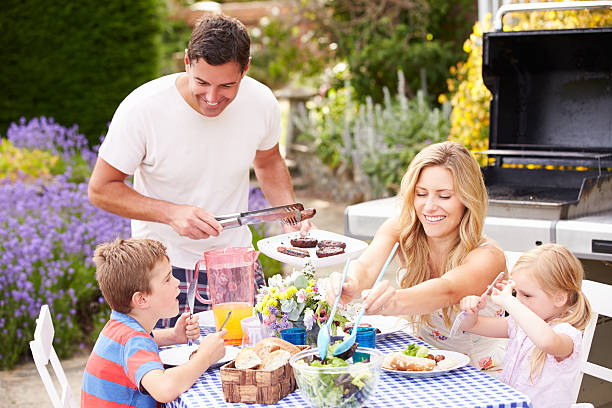 Family Enjoying Outdoor Barbeque In Garden Family Enjoying Outdoor Barbeque In Garden On Sunny Day staycation photos stock pictures, royalty-free photos & images