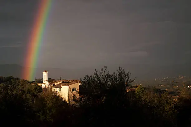 Rainbow over the hamlet of houses and the small bell. In the distance valleys of Tuscany and Florence