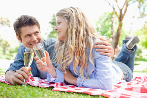 An excited couple celebrate an occasion in the park with wine