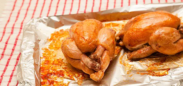 two juicy roasted poussin on aluminium foil from oven