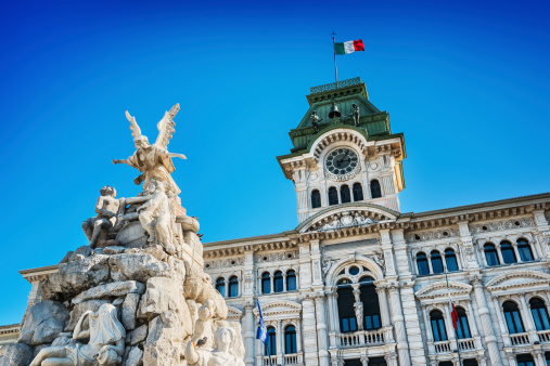 Fountain and The Town Hall in Piazza Unità d'Italia (Unity of Italy Square) at the main square of the northern Italian city of Trieste. Beautiful blue clear sky in the background.