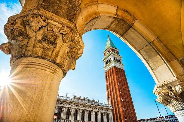 Famous Venetian Palazzo Ducale with view of Piazza San Marco, Venice, Italy. Beautiful view of Venetian tower with column like frame of the photo and sunbeam over the palace.