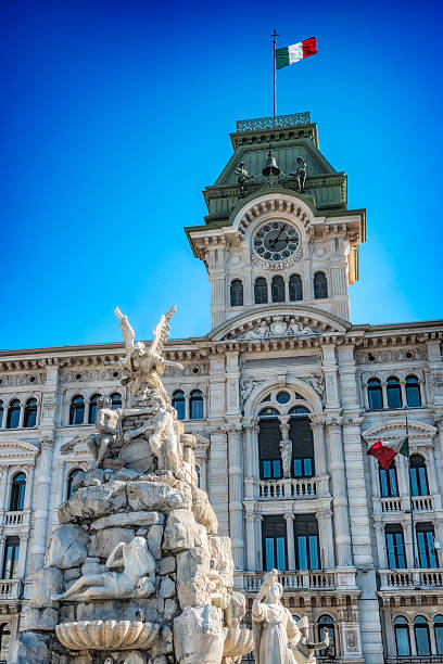 Fountain and The Town Hall in Piazza Unità d'Italia (Unity of Italy Square) at the main square of the northern Italian city of Trieste. Beautiful blue clear sky in the background.