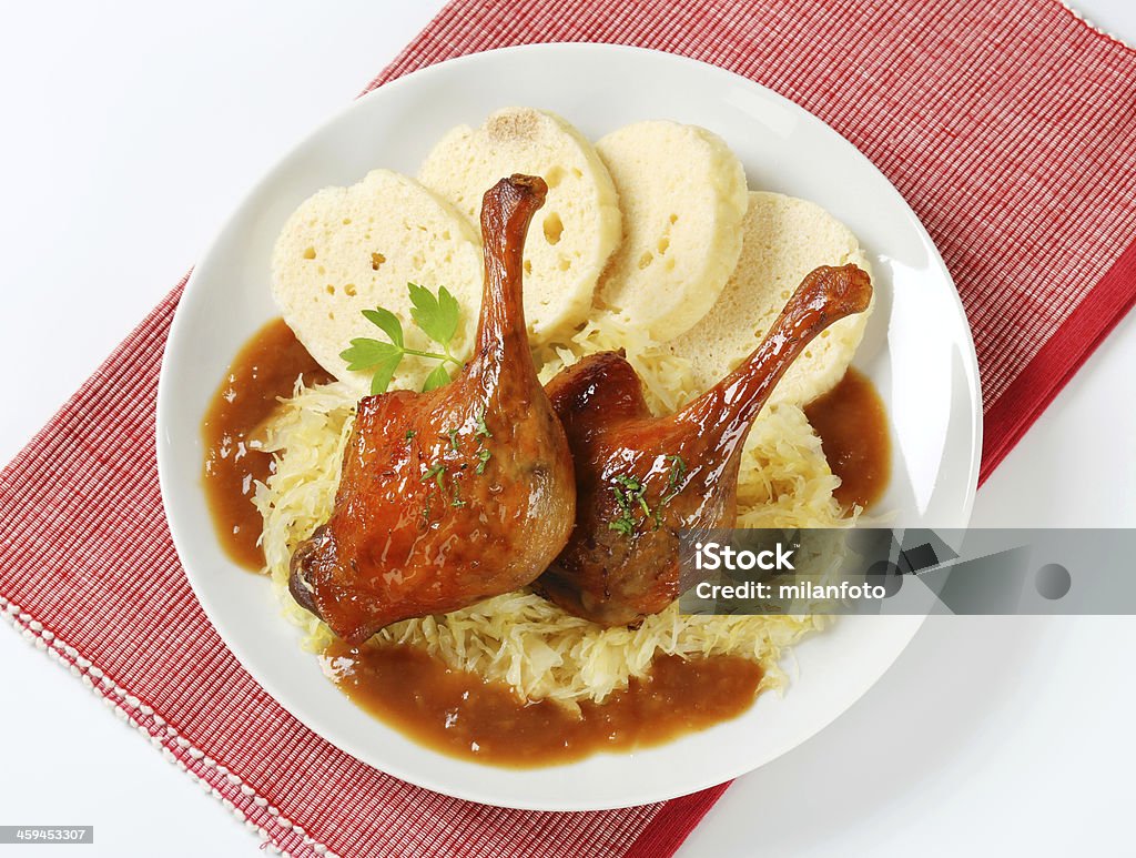 roasted duck, dumplings and cabbage roasted duck legs, bread dumplings and white shredded cabbage on white plate and red placemat Animal Body Part Stock Photo