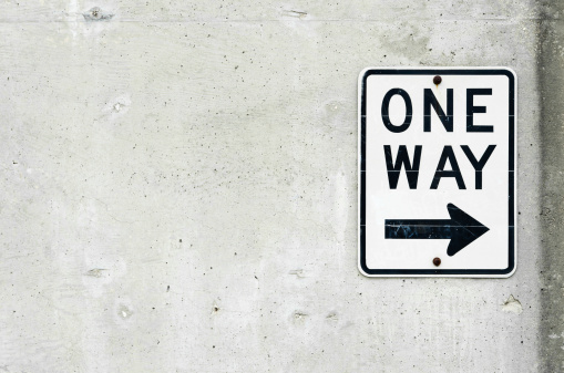 One way sign that points right and is posted on a concrete wall. Composition is horizontal.