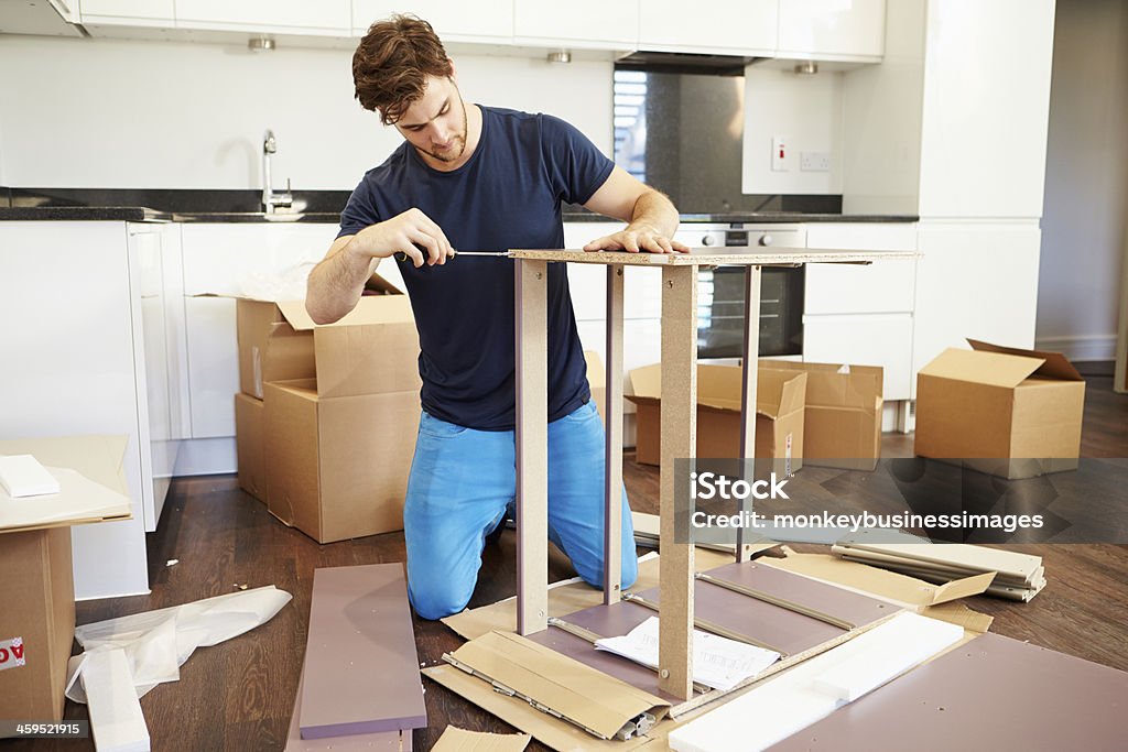 Man assembling furniture in his new home Man Putting Together Self Assembly Furniture In New Home On Both Knees Furniture Stock Photo