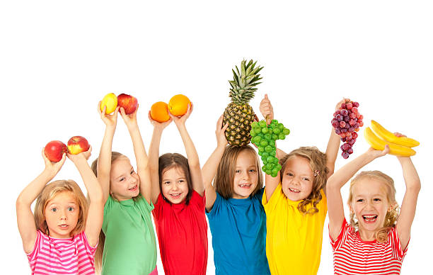 Group of smiling children holding fruits over their heads stock photo