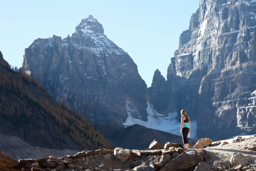 A woman gazes up at a stunning mountain while on a summer hike. Lake Louise, Alberta, Canada.