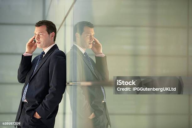 Businessman Using Mobile Phone While Leaning On Glass Wall Stock Photo - Download Image Now