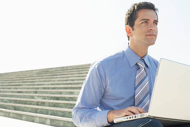 istock Businessman With Laptop Sitting On Staircase Against Sky 459649587