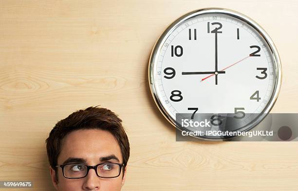 Businessman Looking At Clock On Wooden Wall In Office Stock Photo - Download Image Now