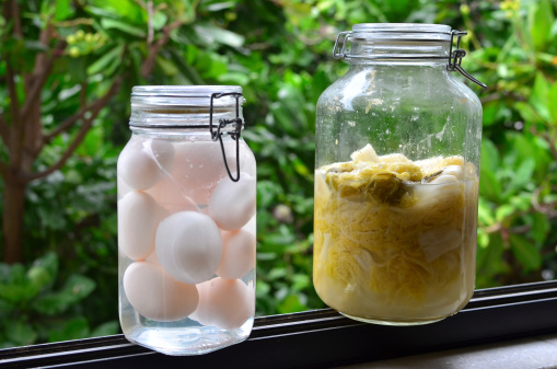 Pickled cabbage and Salty eggs in a glass jar with blurred green leaves at the background