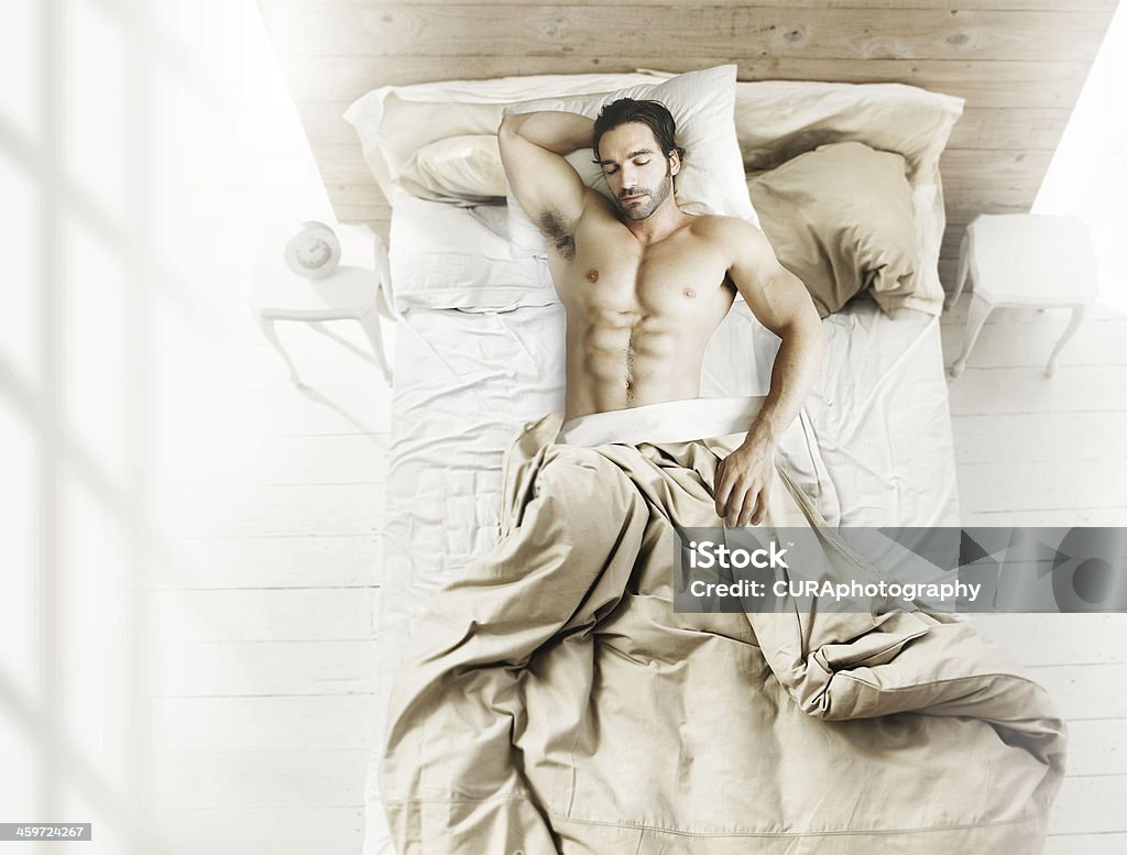 Man in bed from above Portrait of fit male model asleep in luxurious bedroom bathed in bright warm morning window light Men Stock Photo