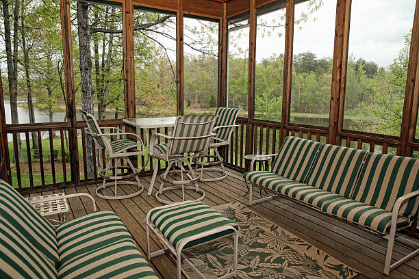 An indoor screened in porch with plants hanging from the side and a tinted yellow glass table with chairs.