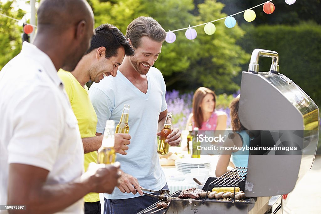 Group Of Men Cooking On Barbeque At Home Group Of Men Cooking On Barbeque At Home In Garden 20-29 Years Stock Photo