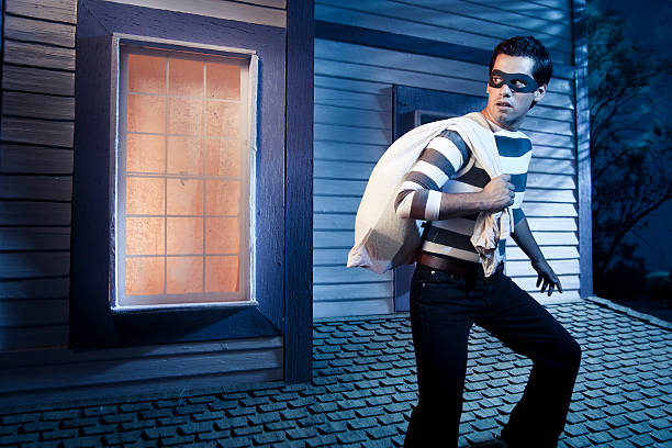 A thief with a bag of loot standing outside a rooftop window