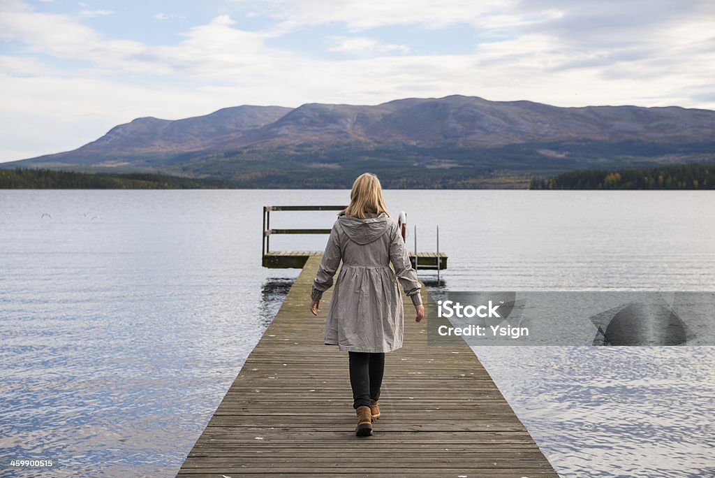 lonely woman walking on a pier lonely woman walking on a pier with a lake and mountains in the background Adult Stock Photo