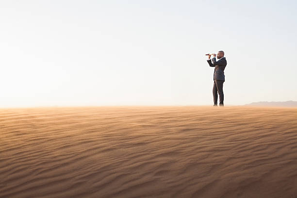 uomo d'affari guardando attraverso il cannocchiale nel mezzo del deserto - arid climate asia color image day foto e immagini stock
