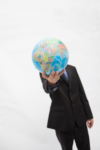 Businessman in a suit holding up a globe in front of his face, obscured face, studio shot
