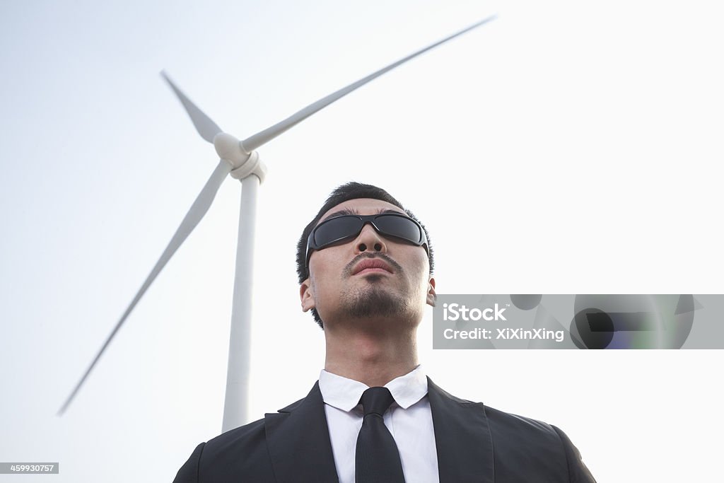 Businessman in sunglasses standing by a wind turbine Portrait of serious young businessman in sunglasses standing by a wind turbine 25-29 Years Stock Photo