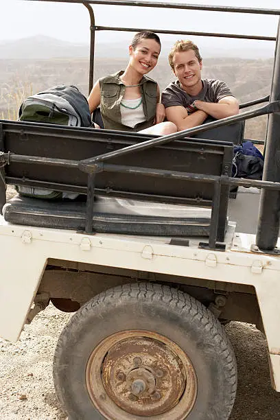 Portrait of happy young couple in stationary four-wheel-drive vehicle in desert