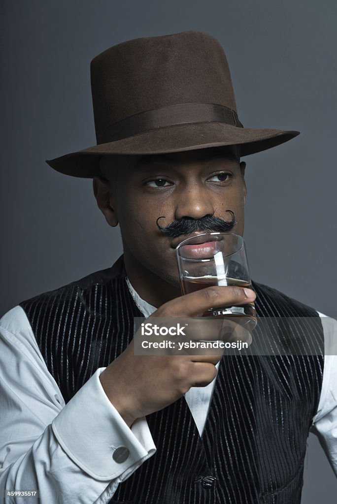 Vintage afro america western cowboy man with mustache. Vintage afro america western cowboy man with mustache. Drinking whiskey. Sitting in wooden chair. Wearing brown hat. Cool tough guy. 1820-1829 Stock Photo