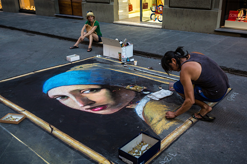 Florence, Italy - July 24, 2013: A street artist draws the Girl with a Pearl Earring, the famous Vermeer painting, on asphalt