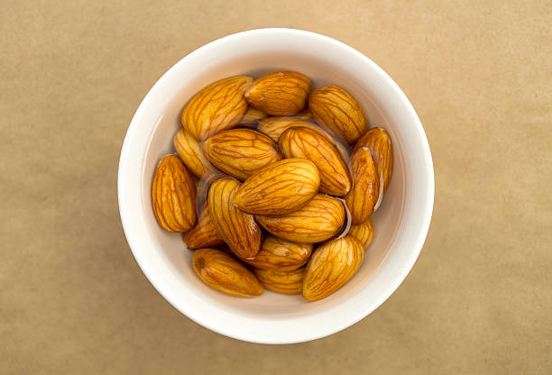 Raw almonds soaking in a white bowl of water Overhead closeup view of raw organic almonds soaking in a white bowl of fresh water drenched stock pictures, royalty-free photos & images