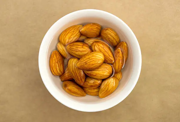 Overhead closeup view of raw organic almonds soaking in a white bowl of fresh water