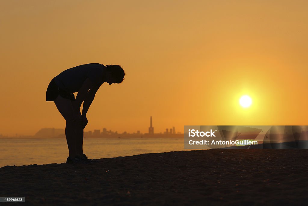 Silhouette of an tired sportsman at sunset Silhouette of an tired sportsman at sunset with a city in the background Heat - Temperature Stock Photo