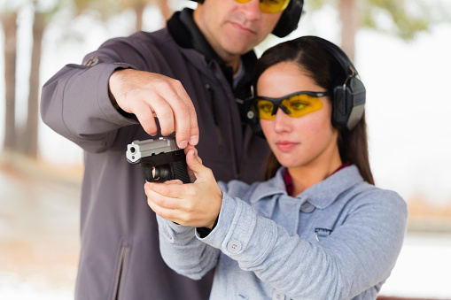 A young woman and instructor practicing at the gun range. Photographed on location at a shooting range.