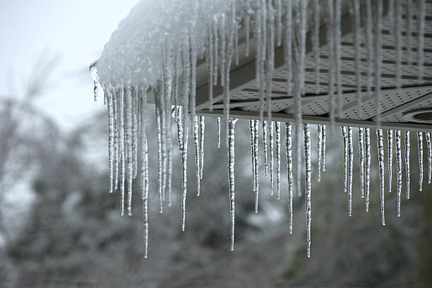 Icicles falling from a roof during winter Icicles forming on the evestrough of a house after a winter ice storm. icicle photos stock pictures, royalty-free photos & images