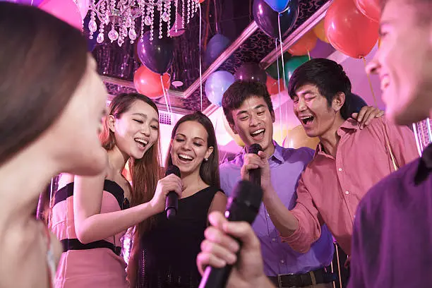 Group of friends holding microphones in a nightclub and singing together karaoke