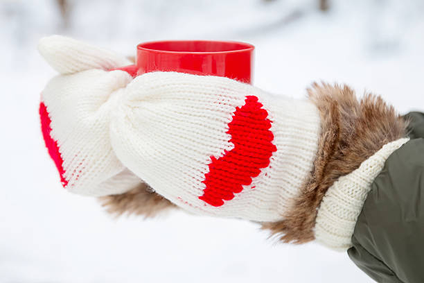 Hands in warm mittens with hearts holding red cup close-upHands in warm mittens with hearts holding red cup close-up