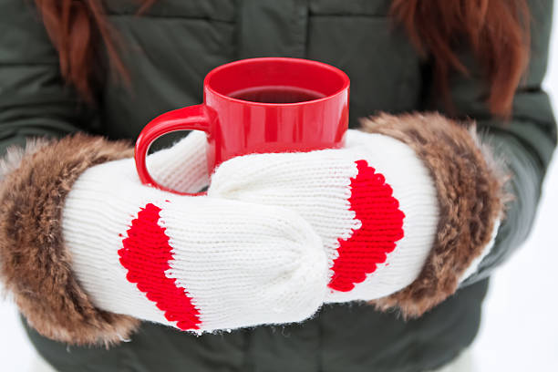 Hands in warm mittens with hearts holding red cup close-up