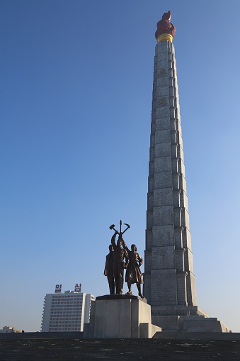 Pyongyang, DPRK - December 22, 2013: The Juche Tower is located In the center of Pyongyang opposite to the Kim Il-Sung Square at the bank of the river Taedonggang. In front of the Juche Tower is a statue with three figures holding hammer, sickle and writing brush. The Juche Tower is named after the principle of Juche.