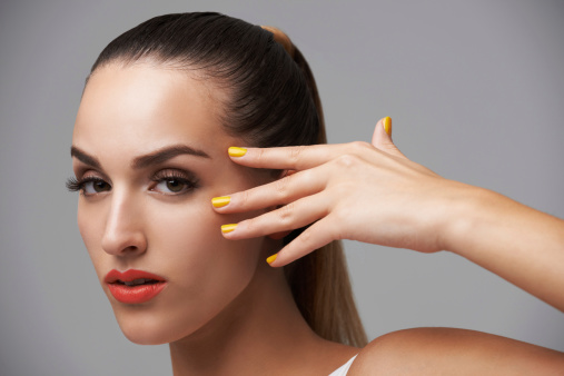 A young woman with colorful nails touching her skin