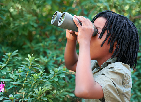Cute little girl exploring nature looking through binoculars. Child playing outdoors. Kids travel, adventure and bird watching concept.