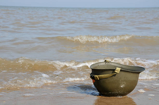 Remember The Fallen A lone WW2 US Army helmet lies upside down on the Normandy beach, a reminder never to forget the fallen. normandy photos stock pictures, royalty-free photos & images