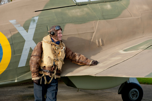 World War Two RAF pilot leaning against a Hurricane fighter aircraft. The pilot is wearing his famous Irvin leather flying jacket with \