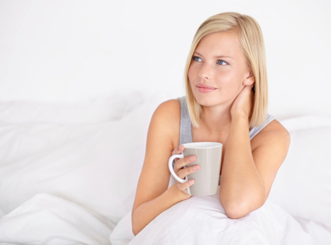 An attractive young woman drinking coffee while sitting in bed