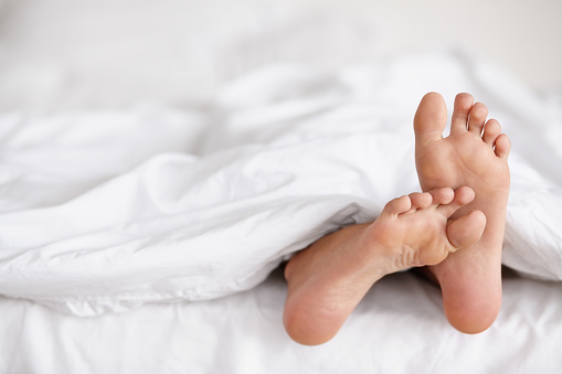 Shot of a pair of woman's feet poking out from under the sheets of a bed
