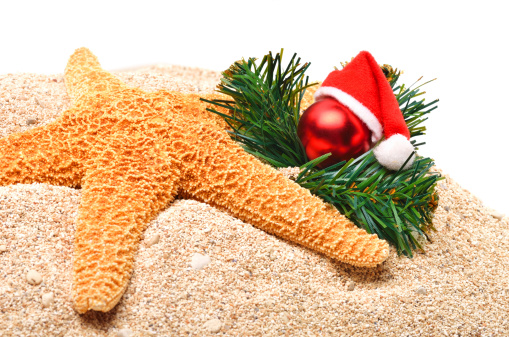 Starfish, christmas baubles and pine twig on the sand isolated on white