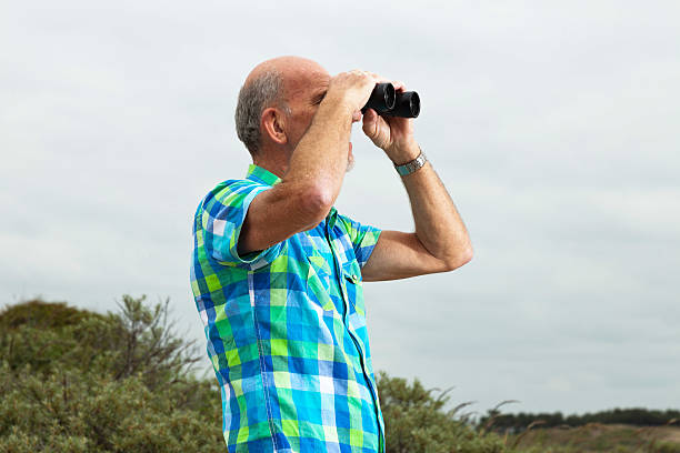 istock Senior man with beard and glasses using binoculars outdoors. 460147861