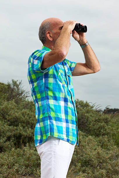 istock Senior man with beard and glasses using binoculars outdoors. 460147887