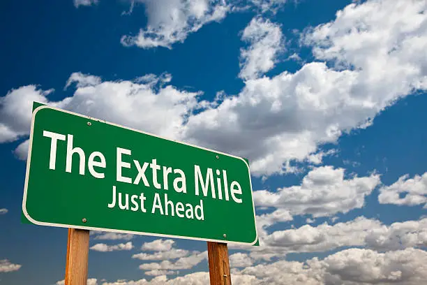 The Extra Mile Just Ahead Green Road Sign Over Dramatic Clouds and Sky.