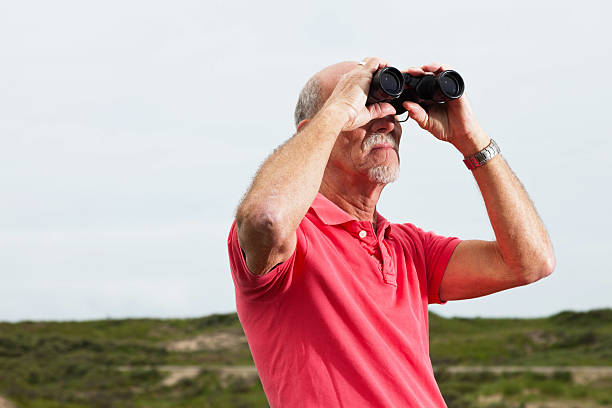 istock Retired man with beard and glasses using binoculars outdoors. 460223941