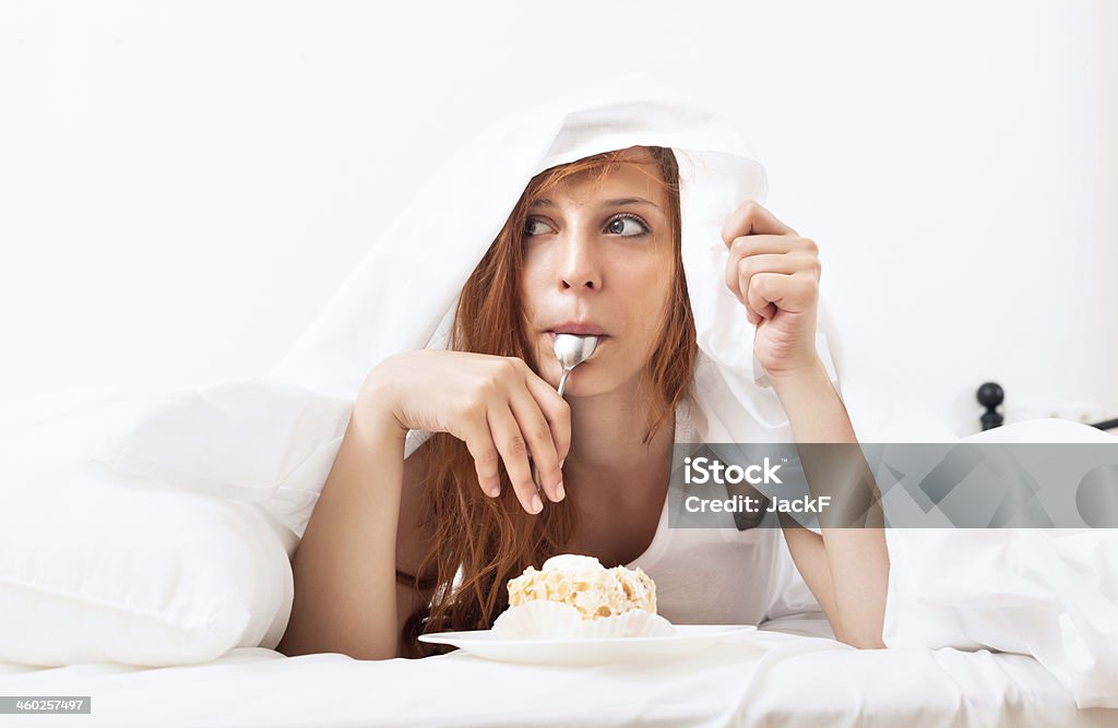 Mujer con cuchara y una porción de pastel en la cama - Foto de stock de Mujeres libre de derechos