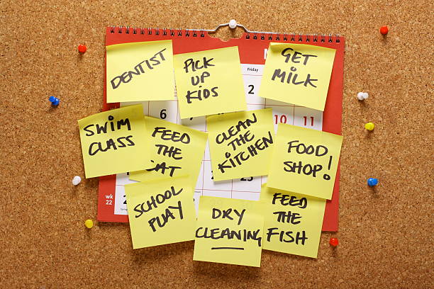 Multitasking Concept A calendar on a cork notice board covered in yellow paper sticky notes with various household chores and errands as a concept for multitasking or being overloaded with housework. busy calendar stock pictures, royalty-free photos & images